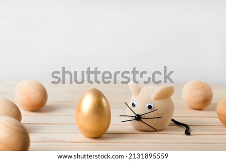 Golden easter egg and toy mouse on wooden surface, easter concept.