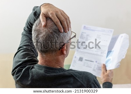 Worried   middle-aged man reading unexpected news in paper document. He is confused and astonished by unbelievable news: high bill tax invoice, debt notification, bad financial report, money problem Royalty-Free Stock Photo #2131900329