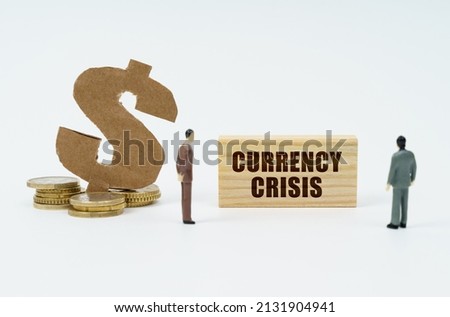 Economy and finance concept. On a white background, coins, a dollar symbol and figures of businessmen who look at a wooden plate with the inscription - currency crisis