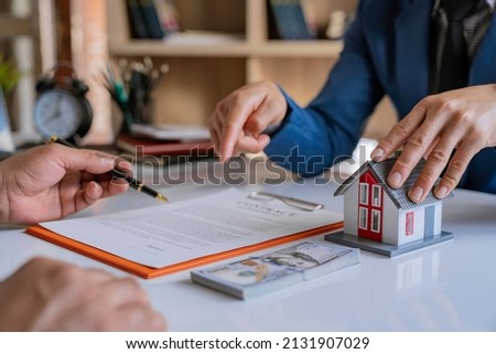 Real estate broker agent presenting and consult to customer to decision making sign insurance form agreement, home model, concerning mortgage loan offer for and house insurance. Royalty-Free Stock Photo #2131907029