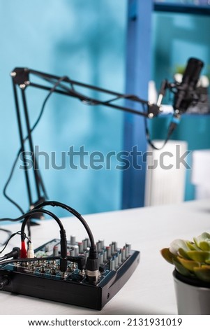 Professional audio mixer used for recording audio podcast on desk in empty vlog studio with swivel mount boom arm microphone. Digital console equilizer used to broadcast live stream.