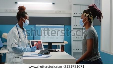 African american medic and patient looking at virus animation on digital tablet while wearing face masks for protection. Black doctor explaining bacteria and disease of coronavirus for woman