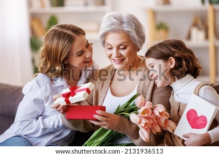 Happy International Women's Day.  multi generational family daughter and granddaughter giving flowers  and gift to grandmother  cheerfully celebrate the spring holiday Mother's Day or grandparents day