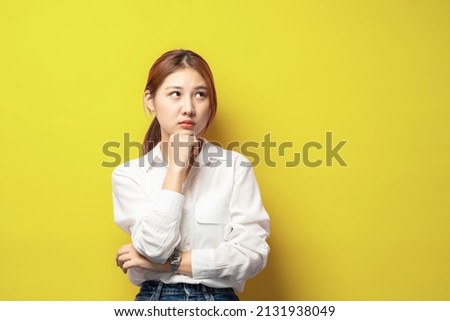 Portrait of thoughtful smart asian woman thinking, female student solving puzzled, look up complicated or pondering, touch chin while trying made up idea, daydreaming over yellow background.