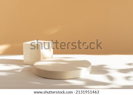 Wooden geometric podium for product demonstration. 3d round and square shapes on white and beige background with floral shadow. Stands for presentation of cosmetics.