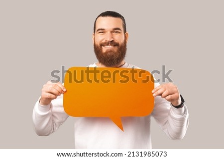 Cheerful bearded man is holding an orange speech bubble in front of him over white background.