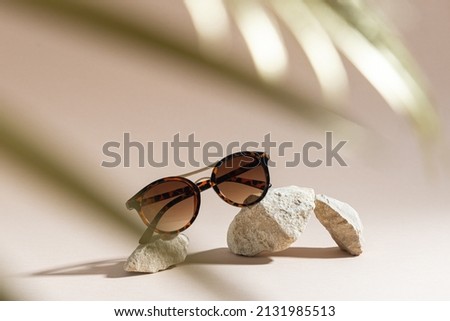 Womens Tortoiseshell frame sunglasses on a beige background with golden palm leaf. Trendy sunglasses still life in minimal stile. Summer fashionable accessories. Optic store discount, sale. Close up Royalty-Free Stock Photo #2131985513