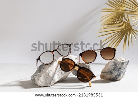 Trendy sunglasses of different design and eyeglasses on gray background with golden palm leaf. Copy space. Sunglasses and spectacles sale concept. Optic shop promotion banner. Eyewear fashion Royalty-Free Stock Photo #2131985531
