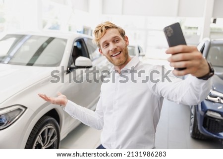 Man customer male buyer client in white shirt do selfie shot on mobile cell phone show car choose auto want buy new automobile in showroom vehicle dealership store motor show indoor. Sales concept.