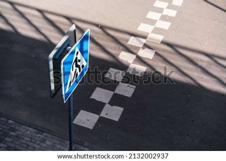 Blue and white sign fixed on pole standing on sidewalk near pedestrian crosswalk. Street safety and signal traffic concept.
