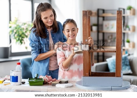 furniture renovation, diy and home improvement concept - happy smiling mother and daughter sticking adhesive tape to old wooden table for repainting it Royalty-Free Stock Photo #2132013981