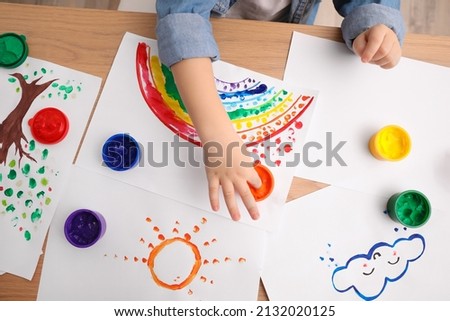 Little child painting with finger at wooden table indoors, top view