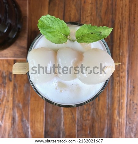 The Lychee skewer and mint leaf on top of the glass of fruity juice put on the wooden table.