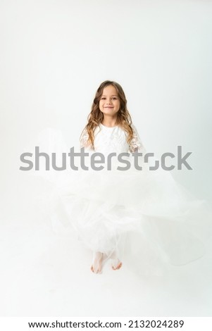 A six-year-old girl in a white dress posing in the studio on a white background