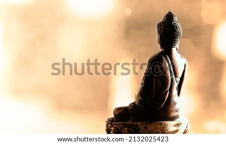 Back side of meditating Buddha statue. Bokeh background. Warm colors. Peace of mind concept