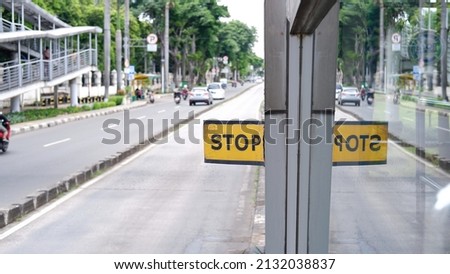 Stop sign board with yellow background and reflection in the glass window 