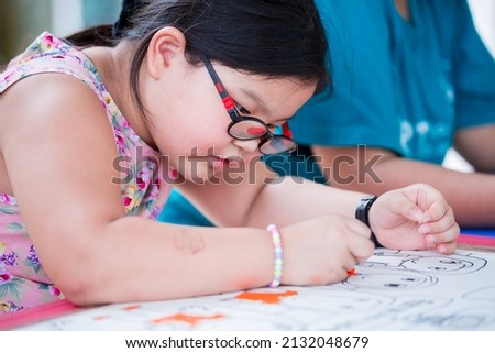 Portrait cute 6 year old Asian girl wearing eyeglasses. Kid is drawing picture of her imagination in classroom art class.