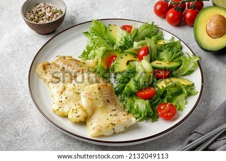 Baked halibut white fish and vegetables salad with green leaves, tomatoes and avocado.