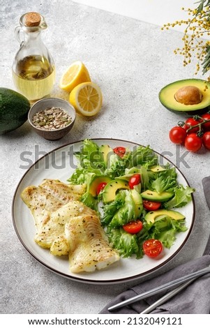 Dish with Gourmet fried halibut fish on Vegetable, fresh green salad. Top view. Black plate. Oli and lemon