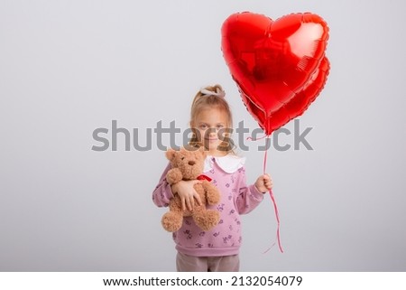  little girl holds balloons in the shape of a heart and teddy bear on a white background, a gift for Valentine's day