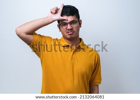 Young handsome man wearing casual shirt standing over white isolated background making fun of people with fingers on forehead doing loser gesture mocking and insulting. Royalty-Free Stock Photo #2132064081