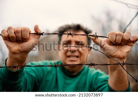 Mature Male hands on barbed wire Struggle for freedom. Man holding metal border fence. Immigration and escape people concept. Refugee trying to cross the border. Close up, selective focus