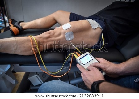 Muscle stimulator device with electrodes applied to quadriceps by a professional physiotherapist Royalty-Free Stock Photo #2132083911