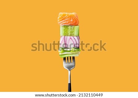 Close-up of fork with food on it: delicious fillet salmon, cucumber, onion, green salad on orange background. Concept of healthy diet and clean eating with fish and vegetables, balanced nutrition Royalty-Free Stock Photo #2132110449