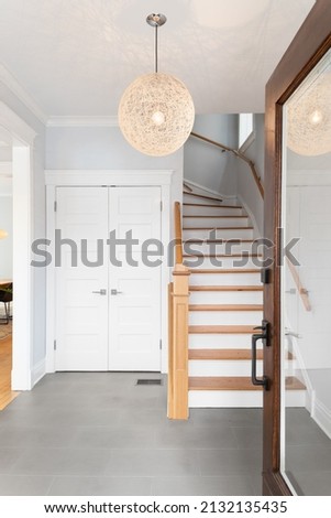Foyer of a home with a wood and glass front door, a hanging light, and looking towards the staircase leading upstairs. Royalty-Free Stock Photo #2132135435