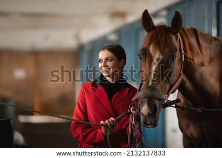 Young woman rider puts on horse saddle in stall.