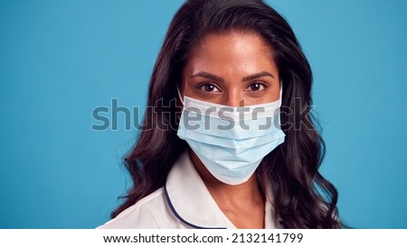 Close Up Of Female Mature Nurse In Uniform Wearing Face Mask In Front Of Blue Studio Background