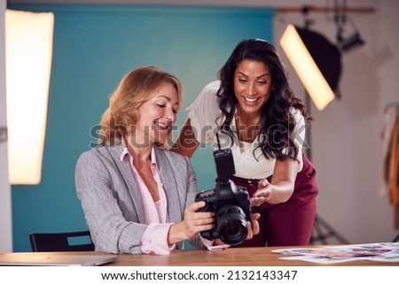 Mature Female Fashion Photographer With Client Looking At Images From Shoot On Camera In Studio