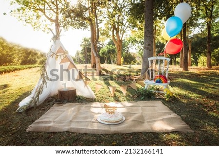 Beautiful birthday party with balloons and garlands in the middle of nature. Birthday party ideas.The cake topping says: "My first lap in the sun"