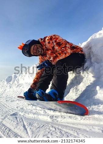A man fastens the fastenings of a snowboard. A snowboarder fastens a snowboard mount before descending a snow-covered ski slope in high mountains on a sunny winter day.