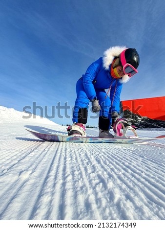 The girl fastens the snowboard fastenings. A snowboarder girl in the snowy mountains, sitting on the snow, fastens the mount and prepares for the descent Royalty-Free Stock Photo #2132174349