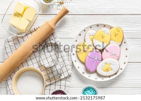 Plate with tasty Easter cookies and ingredients on white wooden background Royalty-Free Stock Photo #2132175987