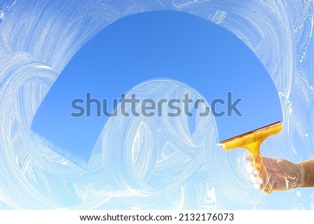 Washing of window with detergent and squeegee against blue sky