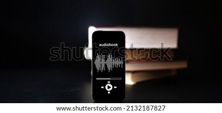 Audiobook education. Smartphone screen with audiobook application on paper books black background. Ebook e learning electronic internet mobility concept