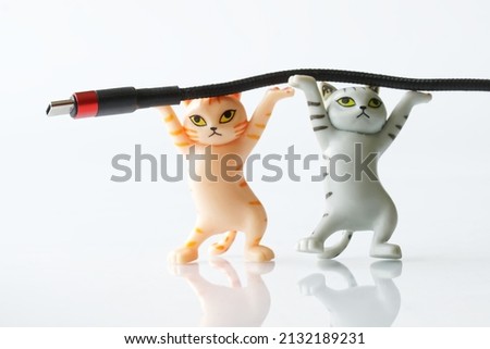 Two cute toy kittens are holding a black wire with a red-black usb type-c connector in their paws. A modern way to transfer digital data and charge gadgets. Copy space for an inscription. Close-up