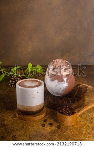 chocolate drink with ice in glass and hot in mug, on rustic wooden tray and authentic background 