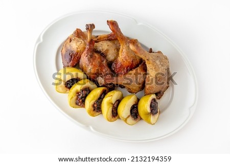 Duck leg confit with baked apples stuffed with dried fruits and nuts on a white plate. Banquet festive dishes. Gourmet restaurant menu. White background.