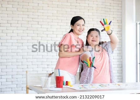 woman teacher and down syndrome girl with painted hands, drawing a picture on table