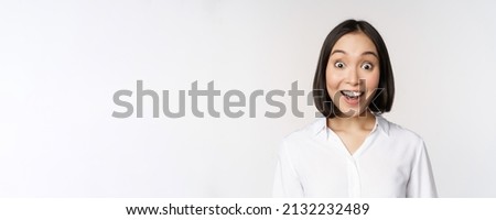 Image of korean woman looking surprised and happy at camera, standing over white background