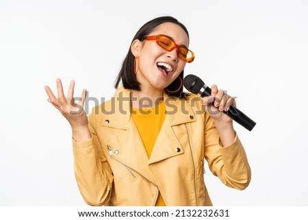 Singing girl holding microphone, performing songs at karaoke, standing over white background Royalty-Free Stock Photo #2132232631