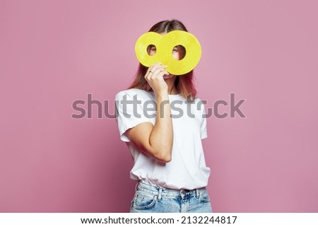 Pretty woman hiding her face behind yellow number eight 8 banner on pink background. Young model in white blank t-shirt