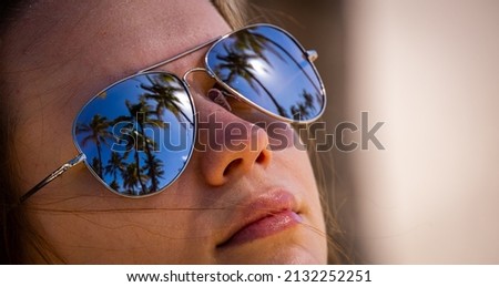 Face of a beautiful girl with sungalsses mirroring palm trees