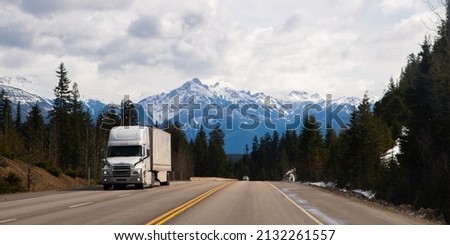 large white transport truck travelling on trans Canada highway in British Columbia Canada with scenic mountains mountaineous scenery in background good winter road conditions horizontal format  Royalty-Free Stock Photo #2132261557