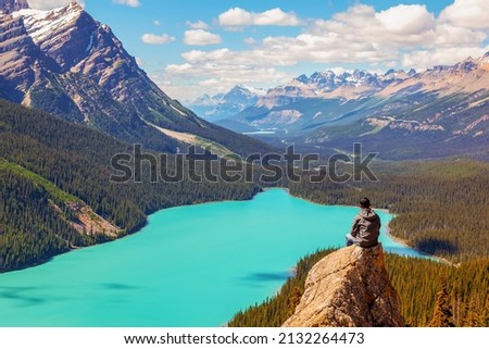 A hiker sits on the peak of Bow Summit with stunning view of Peyto Lake in the Canadian Rockies of Banff. The glacier-fed lake is famous for its bright turquoise colored waters in the summer. Royalty-Free Stock Photo #2132264473