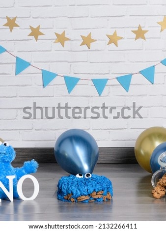 Fantastic cake decorated with blue buttercream icing. Birthday cake with monster and biscuits. Birthdays kids. Golden, blue and glittering balloon background. Fondant baked. Bakery. 1st birthday.
