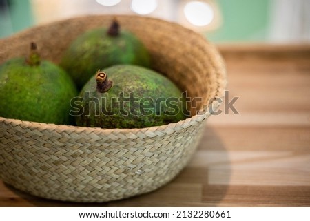 Organic farm avocado in straw basket on wooden table closeup. Fresh ripe green exotic fruits full of healthy nutriment vegetarian eating. Three tropical edible plant with twig for guacamole cooking Royalty-Free Stock Photo #2132280661